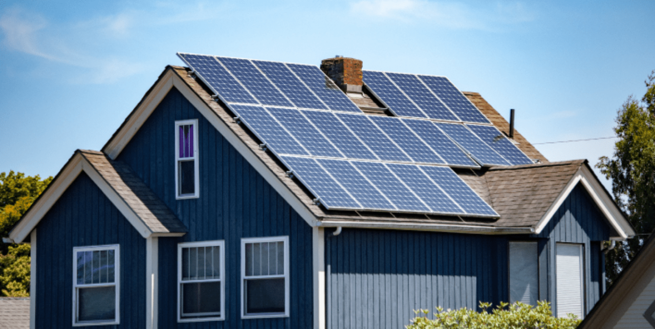 A blue house with solar panels on it's brown roof.